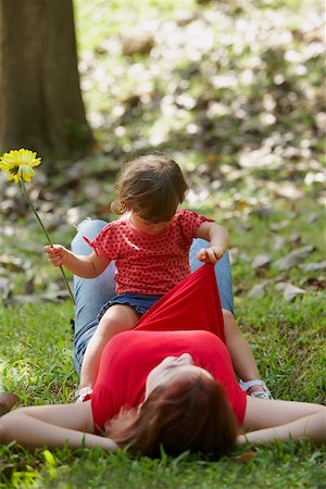 stomach sitting on moms - Young woman lying on grass with her daughter sitting on her stomach Stock Photo - Premium Royalty-Free, Code: 625-01747839