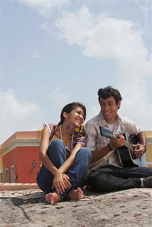 Young man sitting with a young woman and playing a guitar Stock Photo - Premium Royalty-Free, Code: 625-01747842