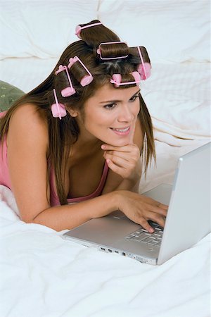 simsearch:625-01747375,k - Jeune femme portant des bigoudis et à l'aide d'un ordinateur portable sur le lit Photographie de stock - Premium Libres de Droits, Code: 625-01748188