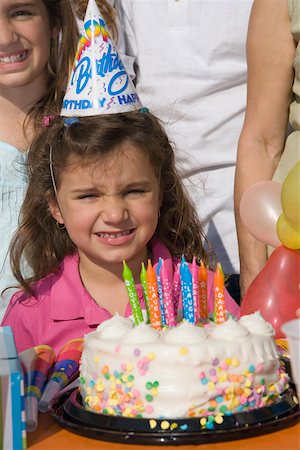 Portrait of a girl with her sisters standing in front of a birthday cake Stock Photo - Premium Royalty-Free, Code: 625-01748251
