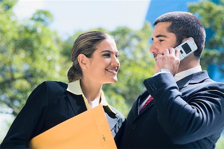 simsearch:694-03327365,k - Homme d'affaires parlant sur un téléphone mobile avec une femme d'affaires souriant à côté de lui Photographie de stock - Premium Libres de Droits, Code: 625-01748328