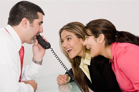 simsearch:625-02931286,k - Side profile of a businessman talking on the telephone with two businesswomen looking at him and smiling Stock Photo - Premium Royalty-Free, Code: 625-01748406
