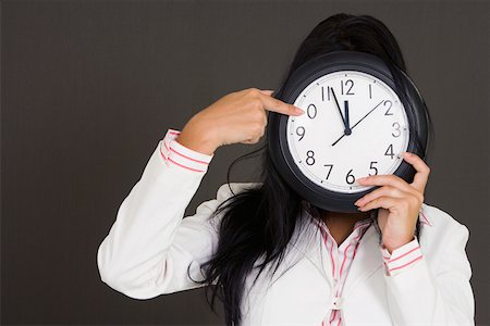 simsearch:625-01748576,k - Close-up of a businesswoman holding a clock in front of her face and pointing Foto de stock - Royalty Free Premium, Número: 625-01748546