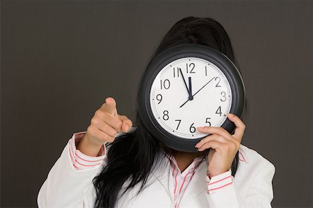 simsearch:625-01748576,k - Close-up of a businesswoman holding a clock in front of her face and pointing Foto de stock - Royalty Free Premium, Número: 625-01748567