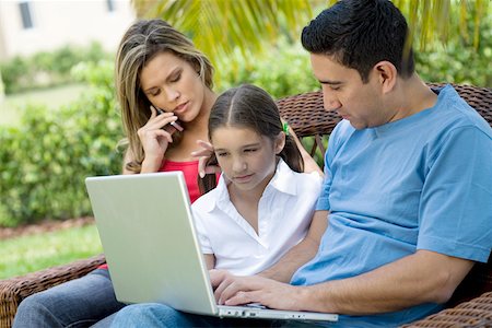 Mid adult man using a laptop with a girl and a young woman sitting beside them Stock Photo - Premium Royalty-Free, Code: 625-01748806
