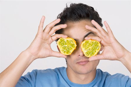 simsearch:625-00838036,k - Gros plan d'un jeune homme fixant les deux moitiés d'un fruit kawani devant ses yeux Photographie de stock - Premium Libres de Droits, Code: 625-01748856