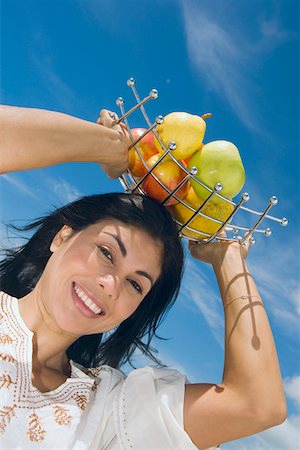 fruits basket low angle - Low angle view of a mid adult woman holding a fruit tray on her head and smiling Foto de stock - Sin royalties Premium, Código: 625-01748857