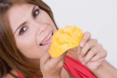 people with fruits cutout - Portrait of a young woman eating cubes of a mango and smiling Stock Photo - Premium Royalty-Free, Code: 625-01748866
