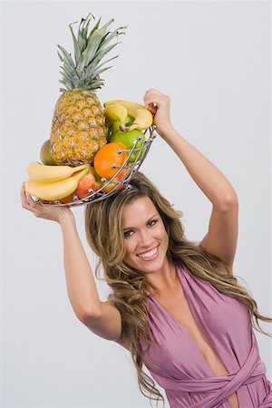 Portrait of a young woman holding a basket of assorted fruits and smiling Stock Photo - Premium Royalty-Free, Code: 625-01748872