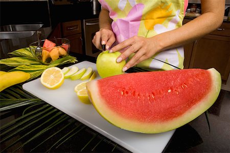 Mid section view of a woman standing at the kitchen counter cutting slices of an apple Stock Photo - Premium Royalty-Free, Code: 625-01748946