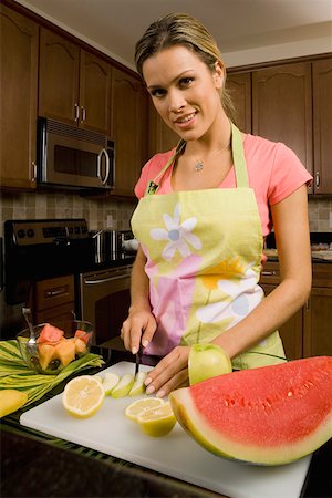 Portrait of a young woman standing at the kitchen counter cutting slices of an apple Stock Photo - Premium Royalty-Free, Code: 625-01748989