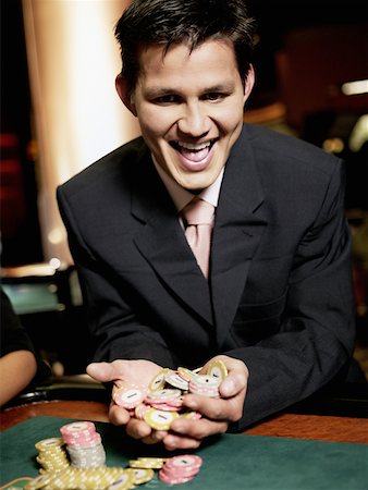 Close-up of a young man cheering with handful of gambling chips in a casino Stock Photo - Premium Royalty-Free, Code: 625-01749130