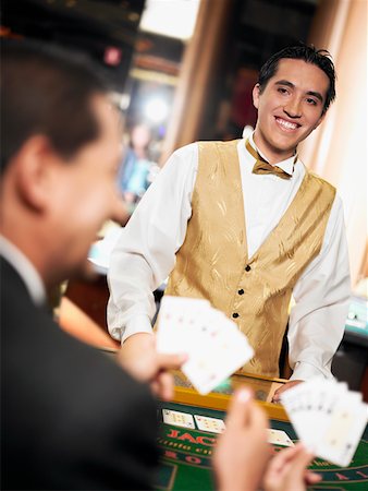 Rear view of a mature man holding playing cards with a casino worker standing in front of him Stock Photo - Premium Royalty-Free, Code: 625-01749169