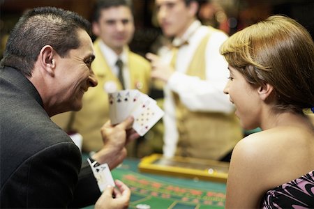 Rear view of a mature man showing playing cards to a young woman in a casino Stock Photo - Premium Royalty-Free, Code: 625-01749175