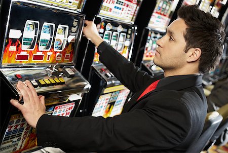 Side profile of a mid adult man playing on a slot machine Stock Photo - Premium Royalty-Free, Code: 625-01749173