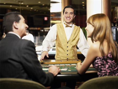 Rear view of a mature man and a young woman sitting at a gambling table with a casino worker smiling in front of them Stock Photo - Premium Royalty-Free, Code: 625-01749180