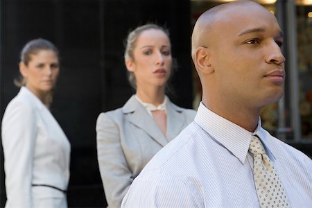 Close-up of a businessman looking serious with two businesswomen standing in the background Stock Photo - Premium Royalty-Free, Code: 625-02266844