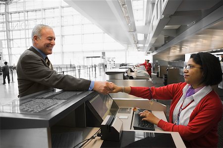 Profil de côté d'un homme d'affaires lui serrer la main avec un agent de bord airline check-in et souriant Photographie de stock - Premium Libres de Droits, Code: 625-02266909