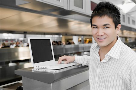 Close-up of a young man using a laptop at an airport and smiling Stock Photo - Premium Royalty-Free, Code: 625-02267057