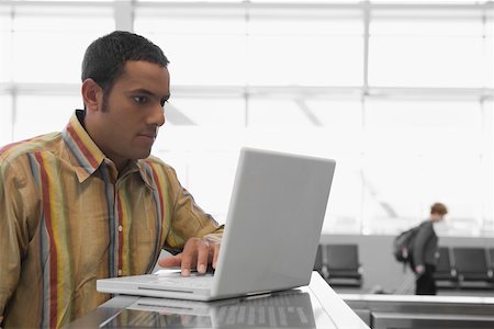 Mid adult man using a laptop at an airport and looking serious Stock Photo - Premium Royalty-Free, Code: 625-02267058