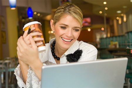 simsearch:625-02267018,k - Femme d'affaires en regardant un ordinateur portable et tenant une tasse jetable dans un restaurant Photographie de stock - Premium Libres de Droits, Code: 625-02267158