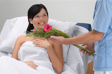 Mid section view of a man giving bouquet of flowers to a patient lying on the bed Stock Photo - Premium Royalty-Free, Code: 625-02267248