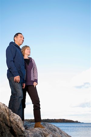 senior couple multicultural - Low angle view of a mature couple standing on a rock and smiling Stock Photo - Premium Royalty-Free, Code: 625-02267673
