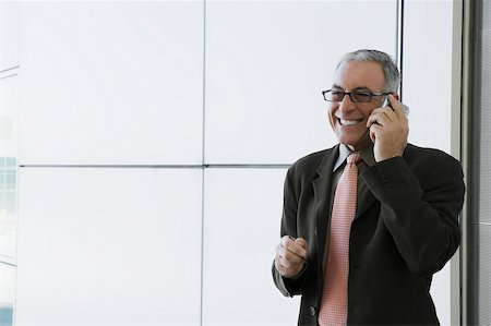 simsearch:625-02933255,k - Homme d'affaires parlant sur un téléphone mobile et souriant dans la salle d'attente d'un aéroport Photographie de stock - Premium Libres de Droits, Code: 625-02929517