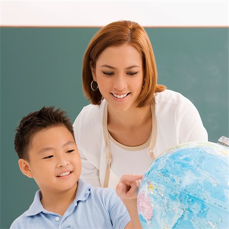 Close-up of a schoolboy with his teacher looking at a globe and smiling Stock Photo - Premium Royalty-Free, Code: 625-02930454