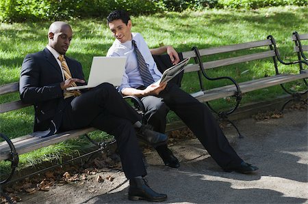 Two businessmen sitting on a bench in a park and looking at a laptop Stock Photo - Premium Royalty-Free, Code: 625-02930797