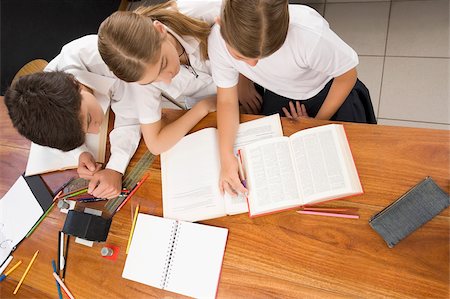 High angle view of two schoolgirls and a schoolboy studying together in a classroom Fotografie stock - Premium Royalty-Free, Codice: 625-02930984