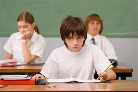 simsearch:625-01249782,k - Schoolboy sitting at a desk with other students in the background Fotografie stock - Premium Royalty-Free, Codice: 625-02930987