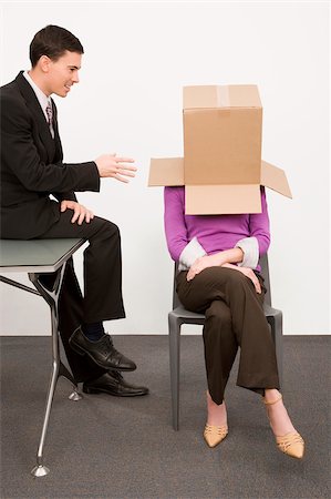 Businesswoman covering her face with a cardboard box and a businessman sitting beside her on a desk Stock Photo - Premium Royalty-Free, Code: 625-02931261