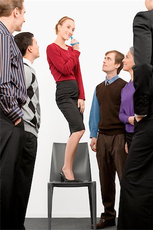 fischiettare - Businesswoman standing on a chair and blowing whistle with business executives standing beside her Fotografie stock - Premium Royalty-Free, Codice: 625-02932269