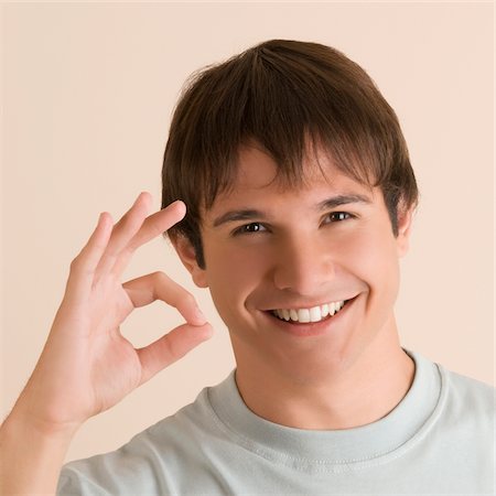 Portrait of a young man showing OK sign and smiling Foto de stock - Royalty Free Premium, Número: 625-02932936