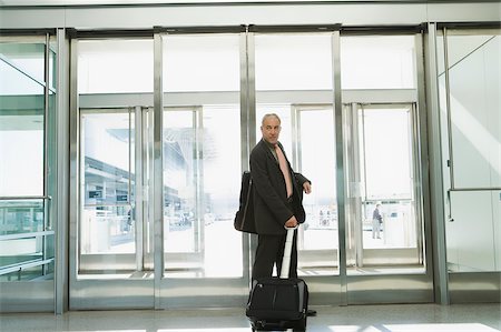 Profil de côté d'un homme d'affaires tirant ses bagages dans un aéroport Photographie de stock - Premium Libres de Droits, Code: 625-02932947