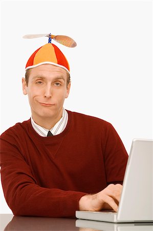 Portrait of a businessman wearing a propeller beanie and working on a laptop Stock Photo - Premium Royalty-Free, Code: 625-02933027