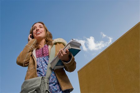 Low angle view of a young woman holding books and talking on a mobile phone Stock Photo - Premium Royalty-Free, Code: 625-02933148