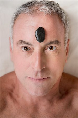 Portrait of a senior man lying on a massage table with a pebble on his forehead Stock Photo - Premium Royalty-Free, Code: 625-02933194