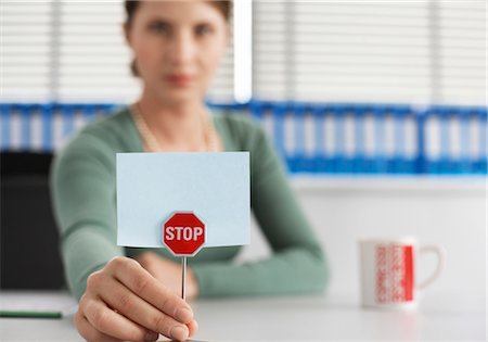 Woman in an office holding a little stop-sign, selective focus Stock Photo - Premium Royalty-Free, Code: 628-05817447