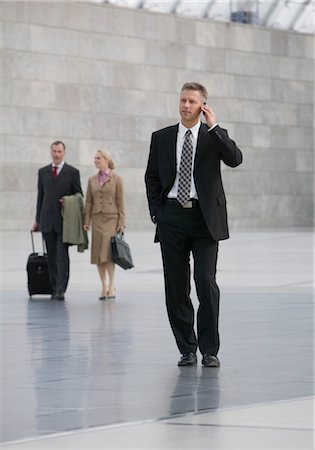 Businessman walking and talking on cell phone, people in the background Stock Photo - Premium Royalty-Free, Code: 628-05817477