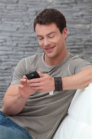 Brunette man in T-shirt using cell phone on couch Stock Photo - Premium Royalty-Free, Code: 628-07072899