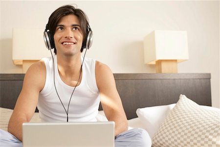 Young man with earphones sitting in front of a laptop Stock Photo - Premium Royalty-Free, Code: 628-00918645