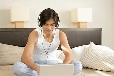 Young man with earphones sitting in front of a laptop Stock Photo - Premium Royalty-Free, Code: 628-00918675