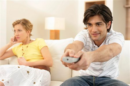 Young man watching TV, bored young woman sitting in background Stock Photo - Premium Royalty-Free, Code: 628-00918696