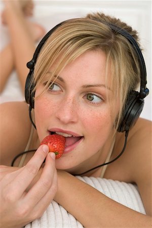 portrait of woman with fruit on head - Femme écoutant la musique par des écouteurs, mange une fraise Photographie de stock - Premium Libres de Droits, Code: 628-00918871