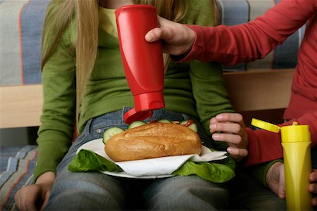 Girl putting ketchup on friend's sandwich Stock Photo - Premium Royalty-Free, Code: 628-00919538