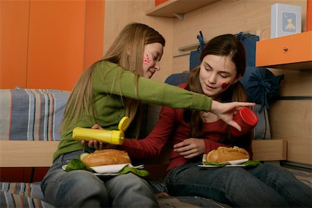 Two friends putting each other ketchup and mustard on sandwiches Stock Photo - Premium Royalty-Free, Code: 628-00919583