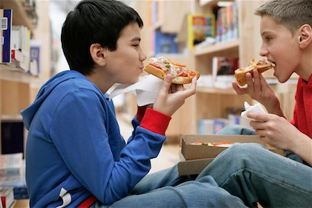 friends and eat and pizza - Two boys eating pizza inside a library, fully_released Stock Photo - Premium Royalty-Free, Code: 628-00919645