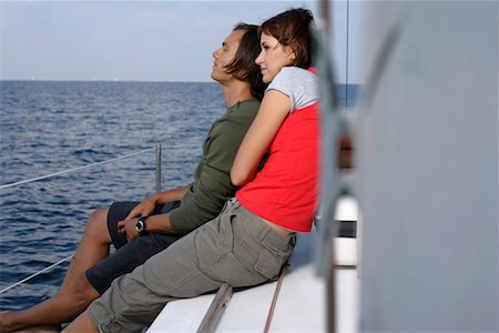 friends sailing - Couple sitting at border of a sailboat, looking over the sea Stock Photo - Premium Royalty-Free, Code: 628-00919946